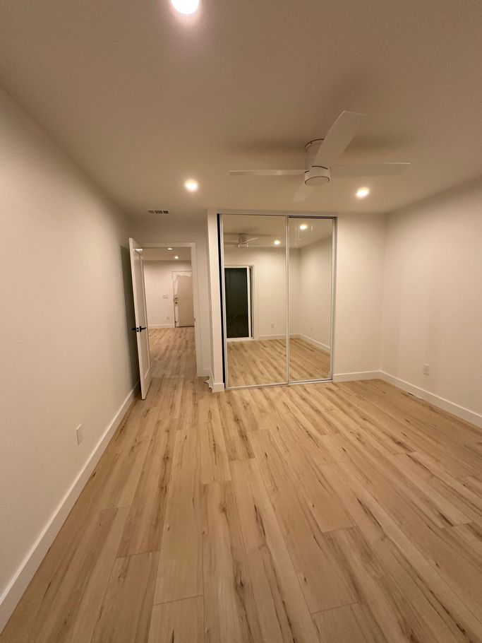 A large empty room with hardwood floors and a ceiling fan.