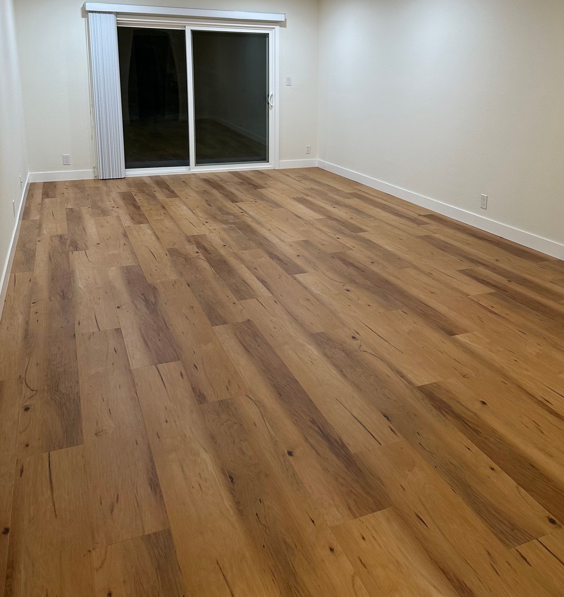 An empty room with a wooden floor and a sliding glass door