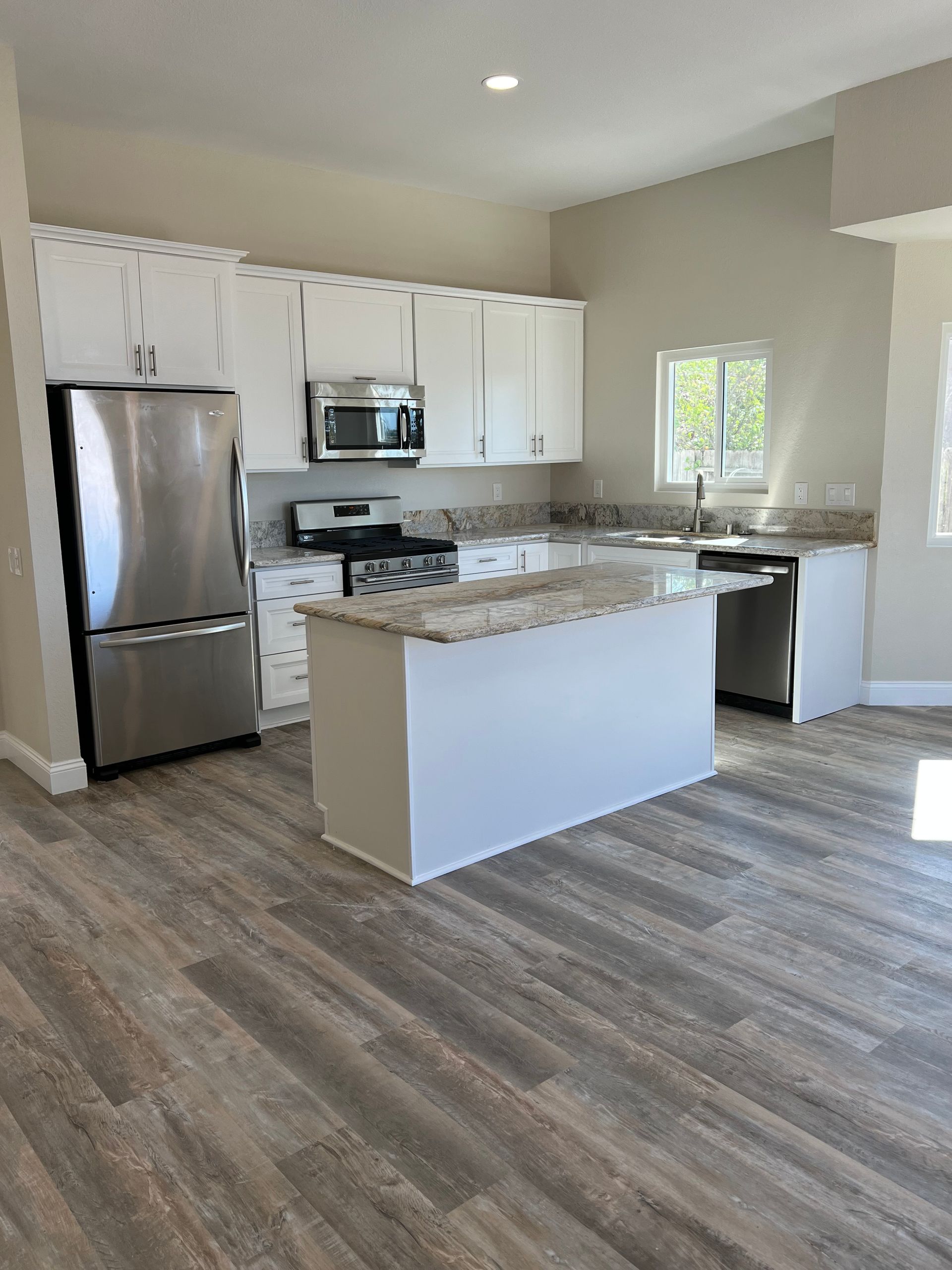 A kitchen with white cabinets , stainless steel appliances , and a large island.