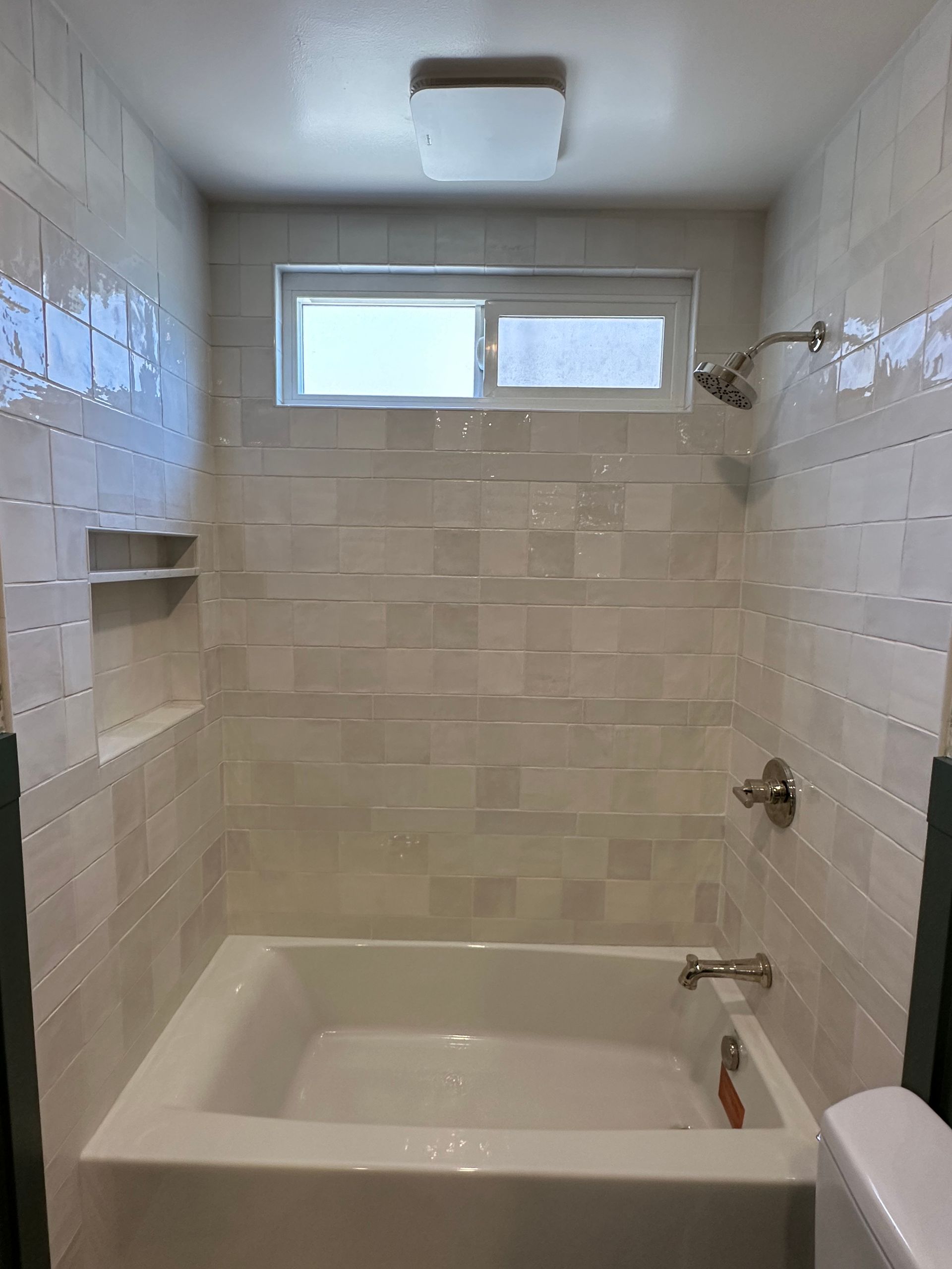 A bathroom with a tub , shower , toilet and window.