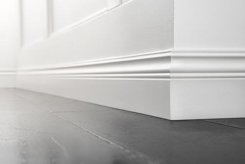 A close up of a white skirting board on a wooden floor.