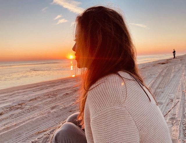 Lori Martorell on beach, looking at sunset over ocean. Warm colors, light reflecting on her face.
