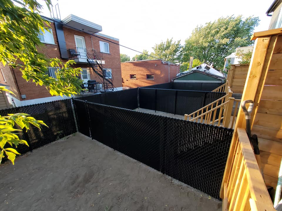 Une clôture à mailles noires entoure une cour arrière avec une terrasse en bois.
