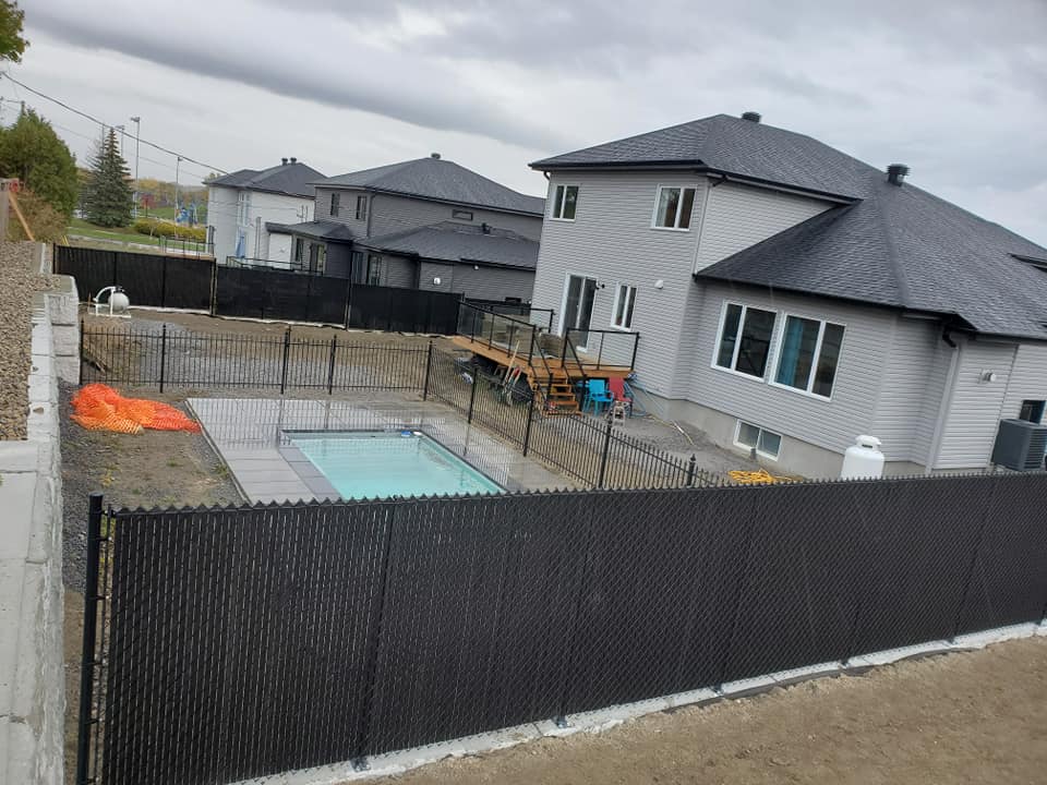 Une grande maison avec une piscine derrière une clôture grillagée noire.