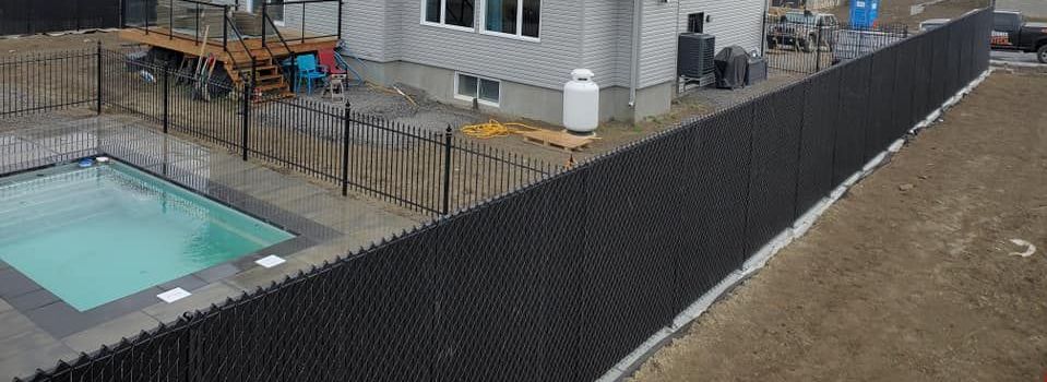 Une clôture noire entoure une piscine devant une maison.