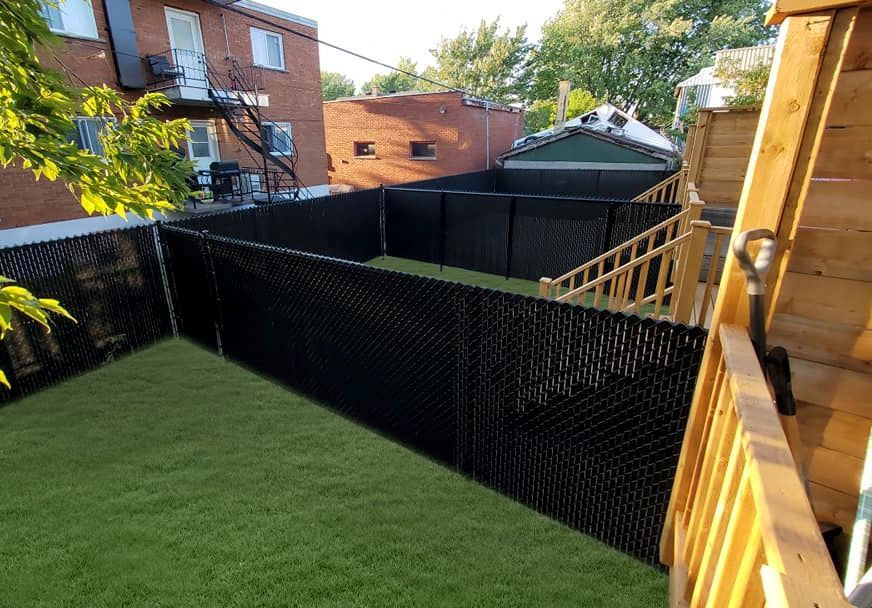 Une cour arrière avec une clôture à mailles noires et une terrasse en bois.