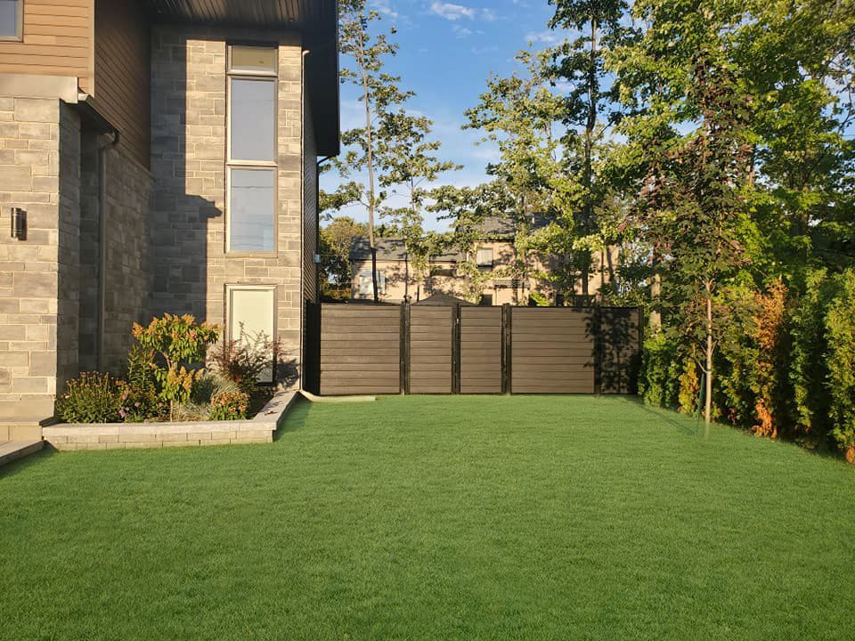 Une grande pelouse devant une maison avec une clôture et des arbres.