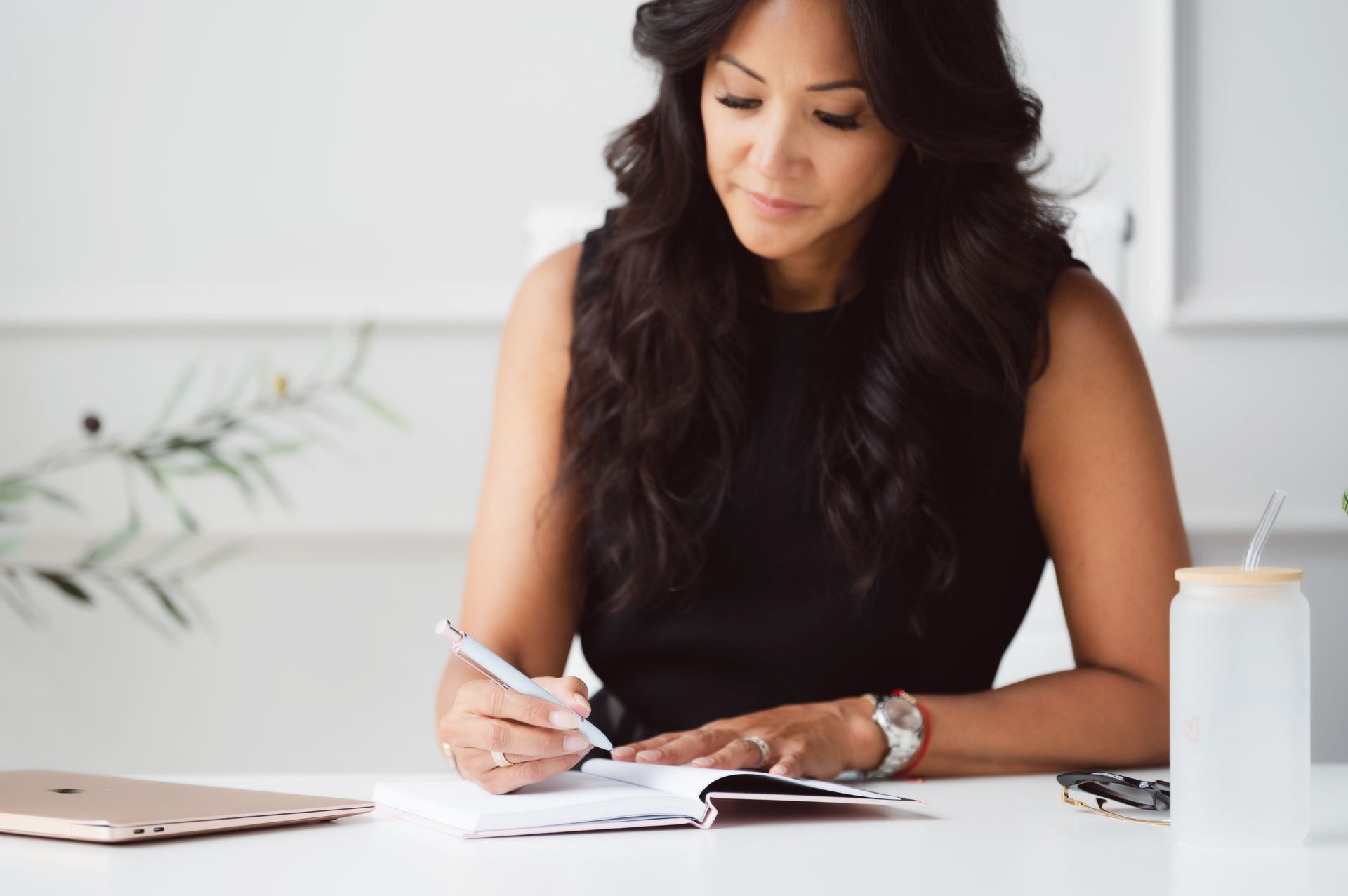 Woman sitting cross-legged near window, writing in a notebook, wrapped in a blanket, bright sunlight.