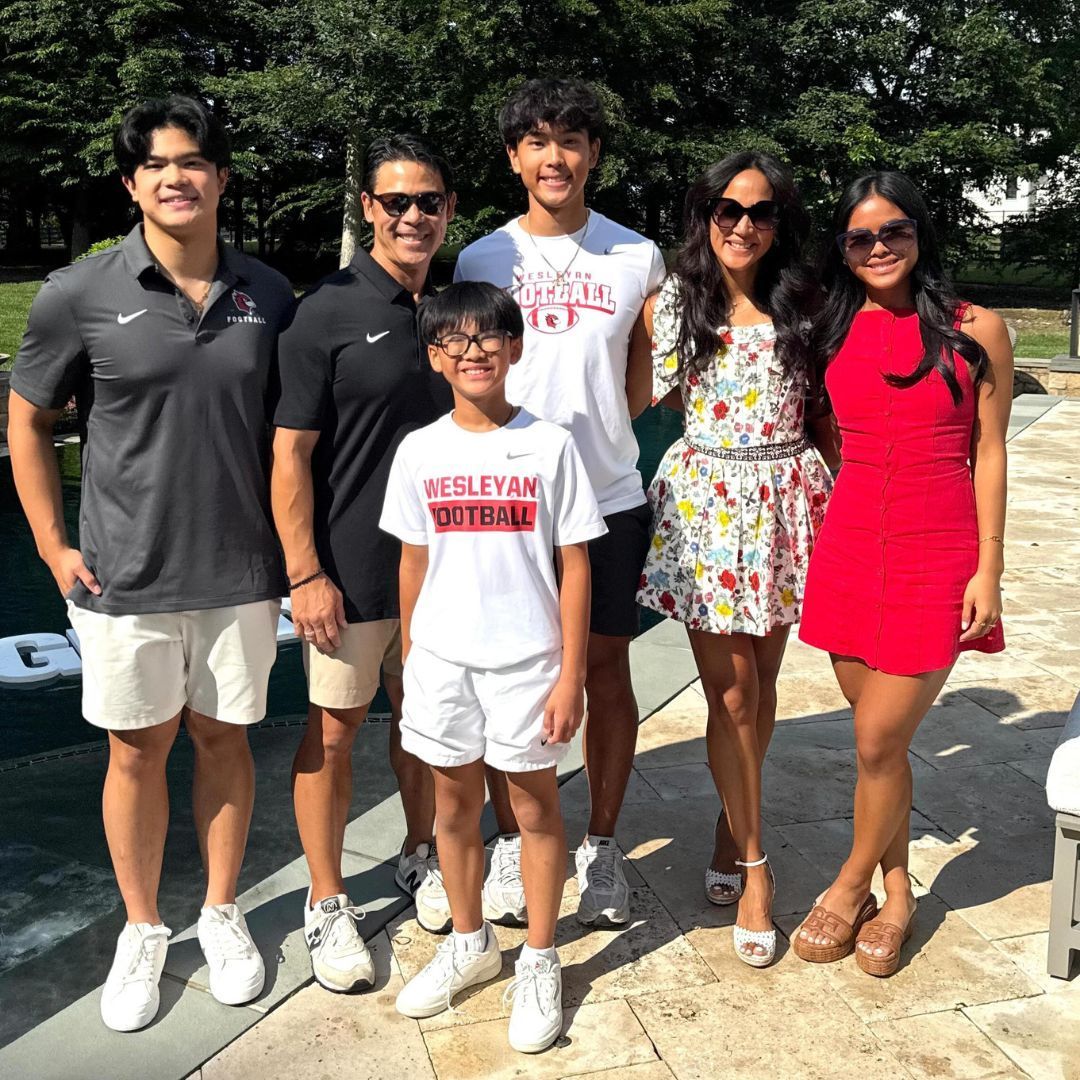 Family of seven smiling, posing by a pool on a sunny day.