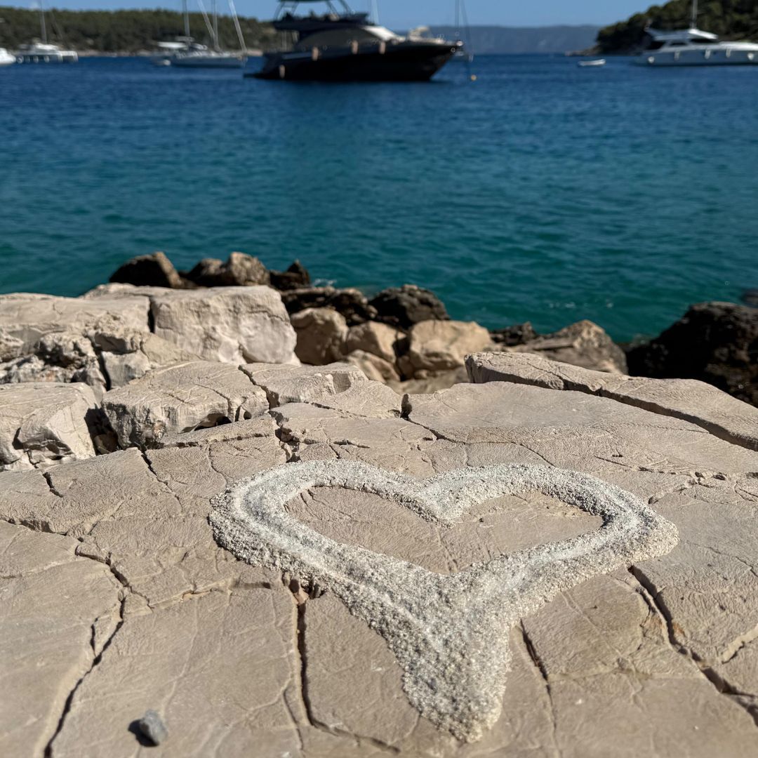 Heart shape drawn in white on a stone surface; boats in a blue sea background.