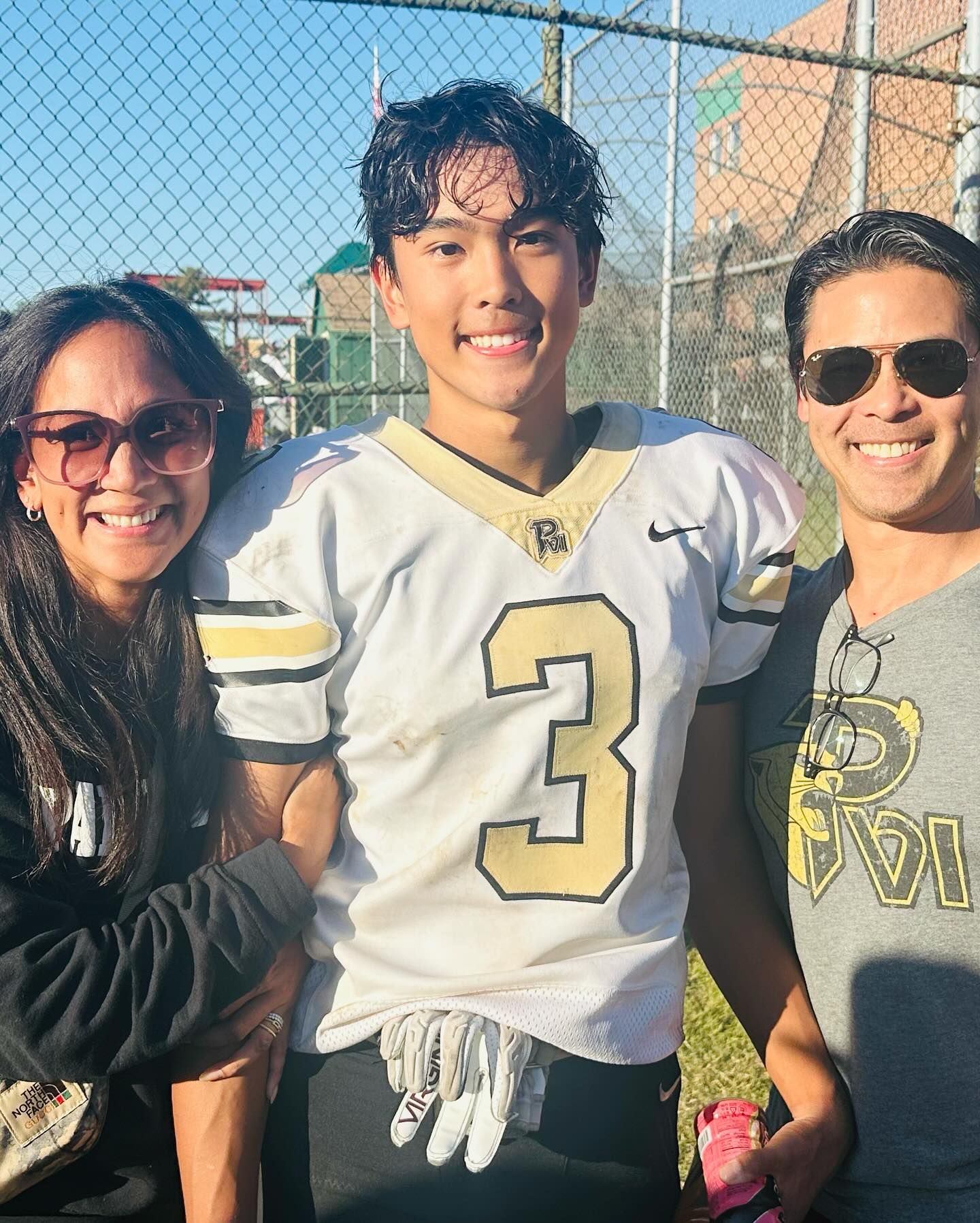 Football player in jersey with parents; smiles for photo, outdoor.