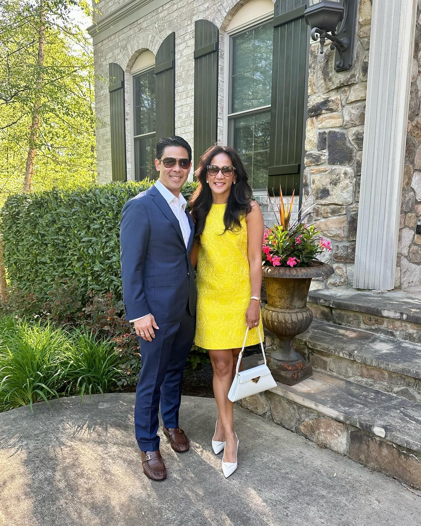 Couple standing by a stone building; the woman wears a yellow dress and the man a blue suit.