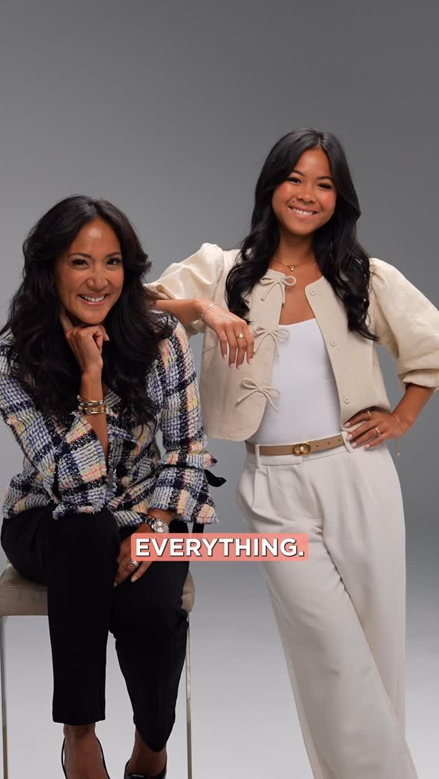 Two women pose, one seated and one standing. They smile. Plain background. Text: 