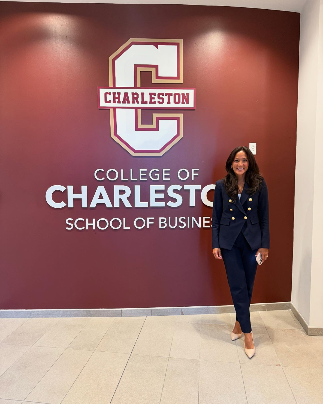 Woman in business attire poses in front of a College of Charleston sign.