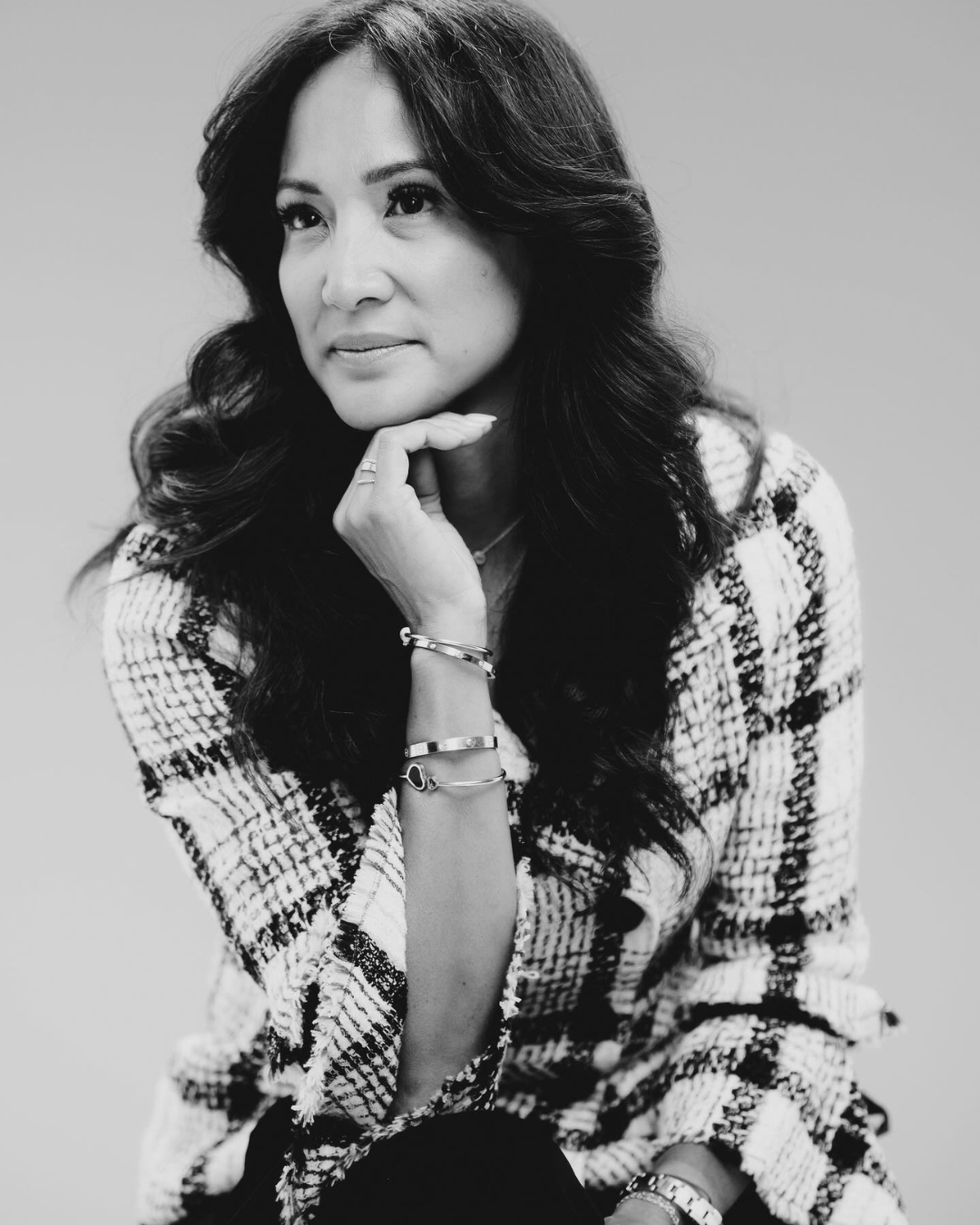 Woman in checkered jacket, hand on chin, looking pensively.