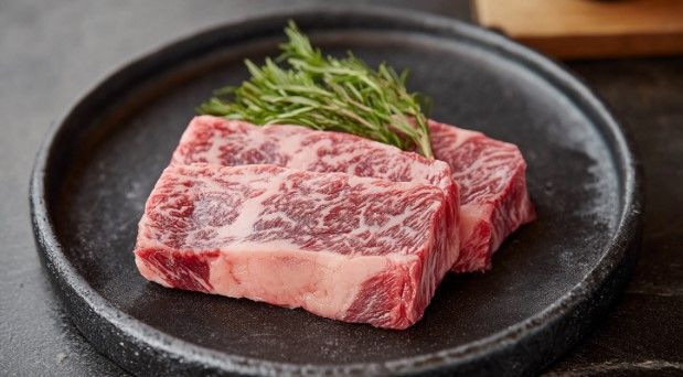 A piece of raw steak on a black plate with a sprig of rosemary.