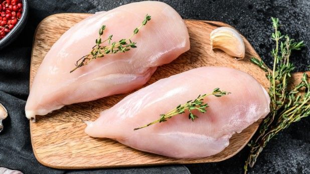 Two raw chicken breasts on a wooden cutting board.