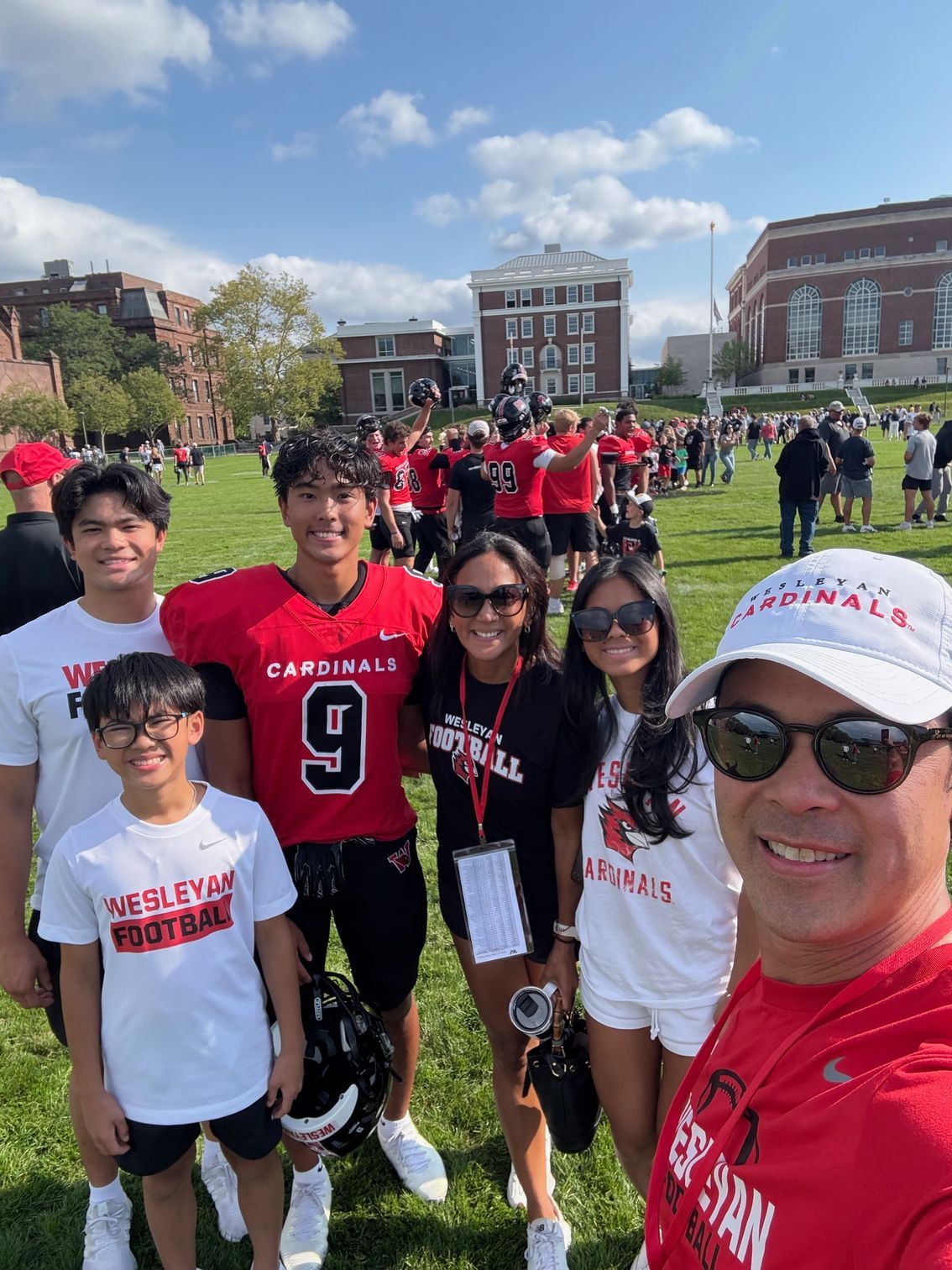 Man giving a thumbs up, carrying a child on his shoulders, both smiling in a park.