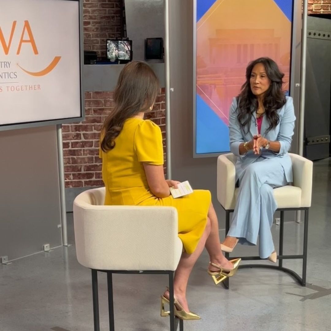 Two women in a studio setting, one in yellow dress interviewing another in a blue suit.