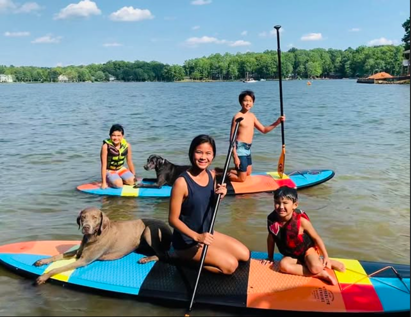 Family and two dogs paddleboarding on a lake under a sunny sky.