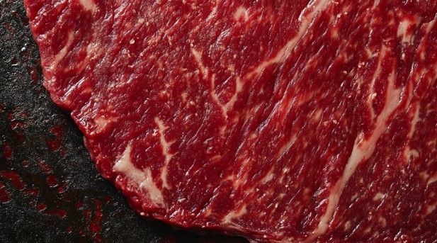 A close up of a piece of raw beef on a black surface.