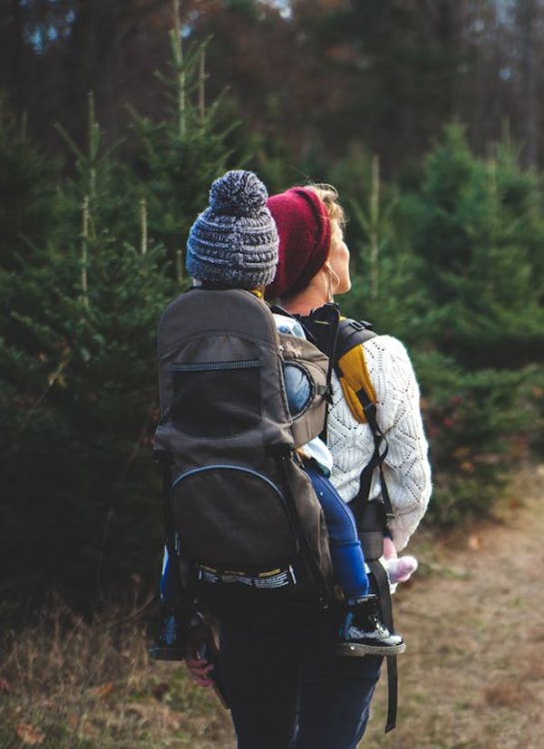 Person carrying a child in a carrier backpack, hiking in a forest.