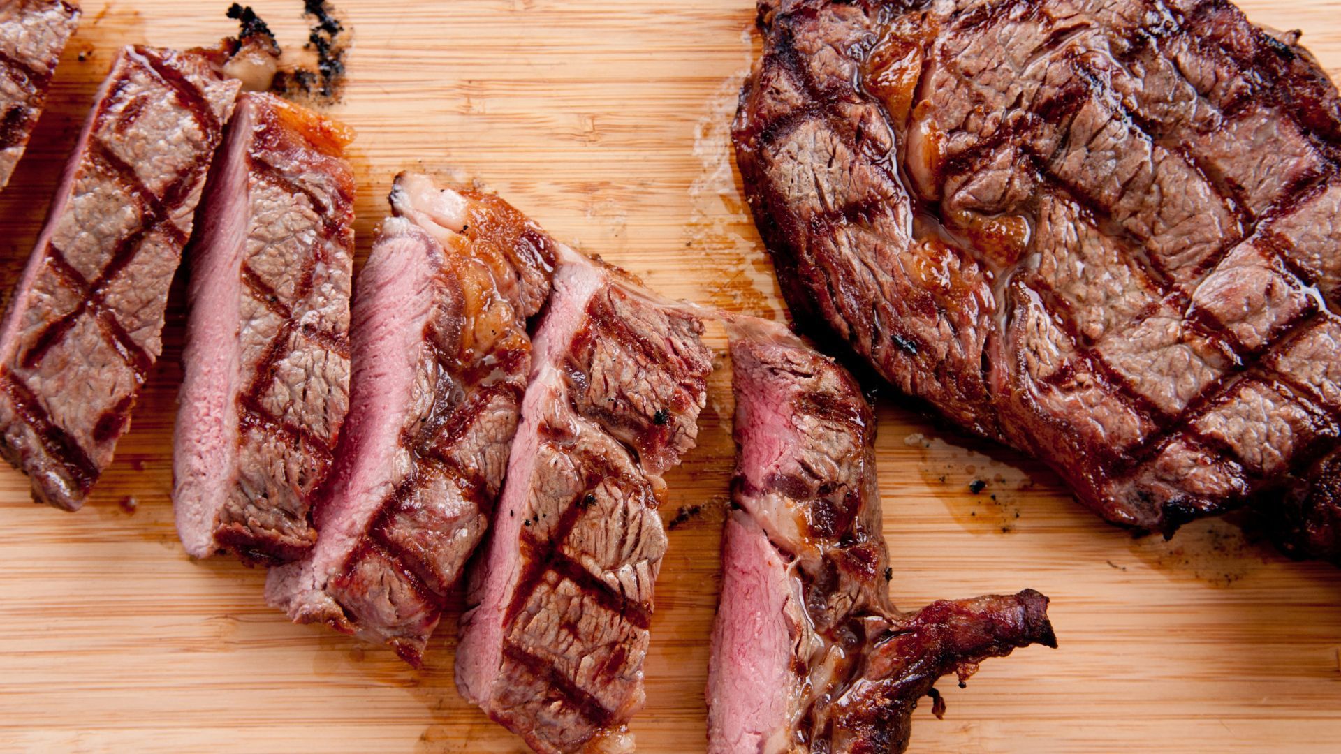 Two grilled steaks are sitting on a wooden cutting board.