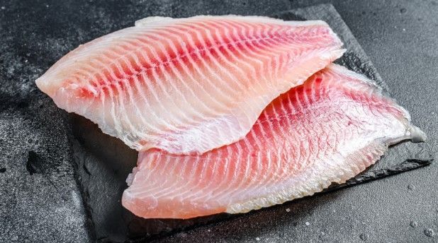 Two pieces of fish are sitting on top of each other on a cutting board.