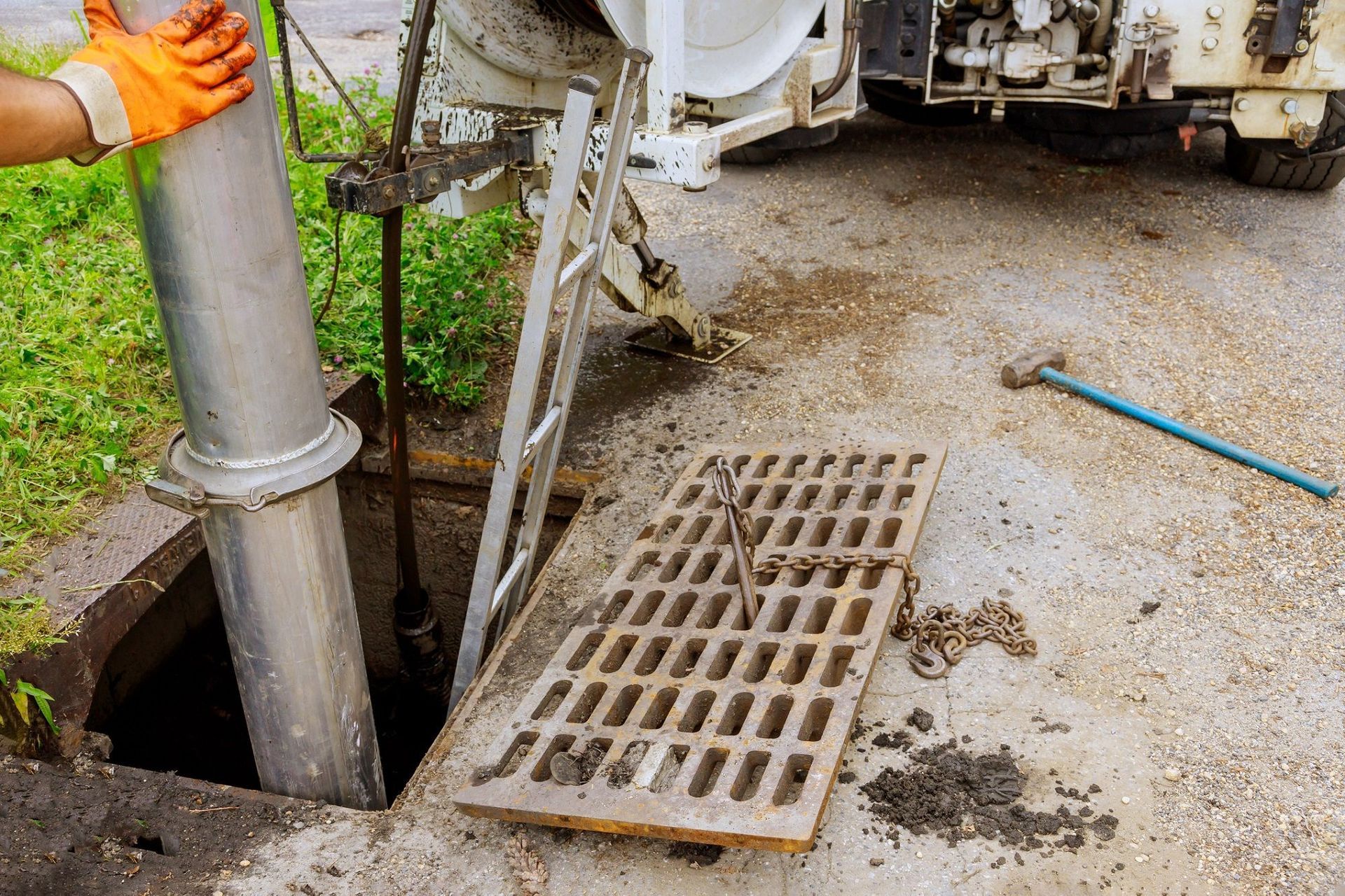 Worker with orange gloves lowers a large pipe into an open sewer grate.