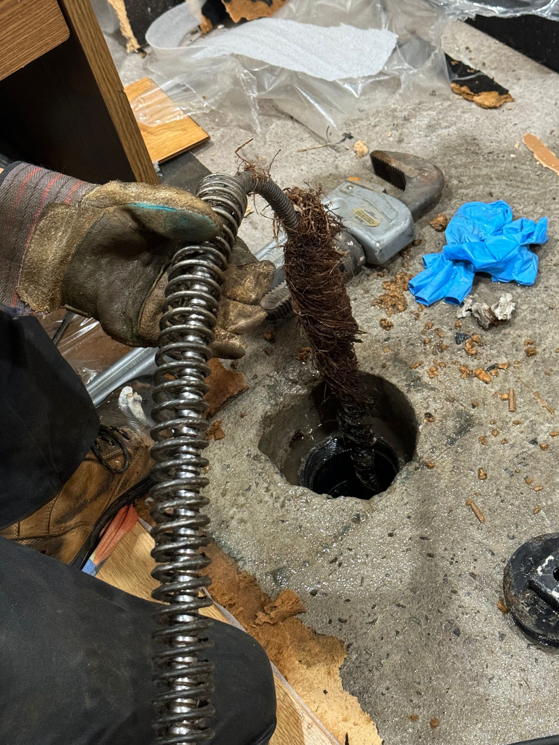 A plumber unclogging a drain with a snake, removing roots; indoor setting.
