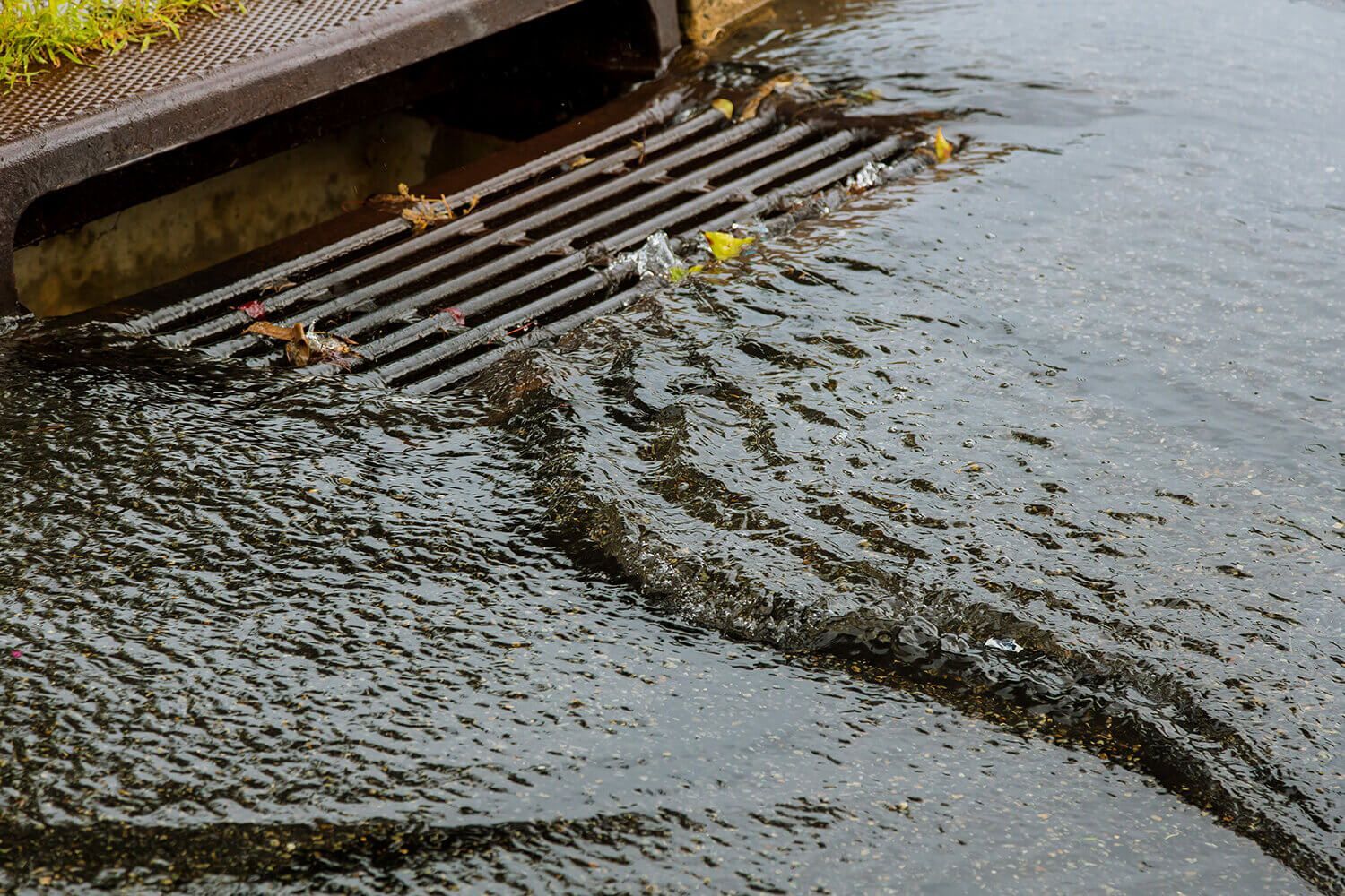 Water overflowing from a storm drain on a wet asphalt road.