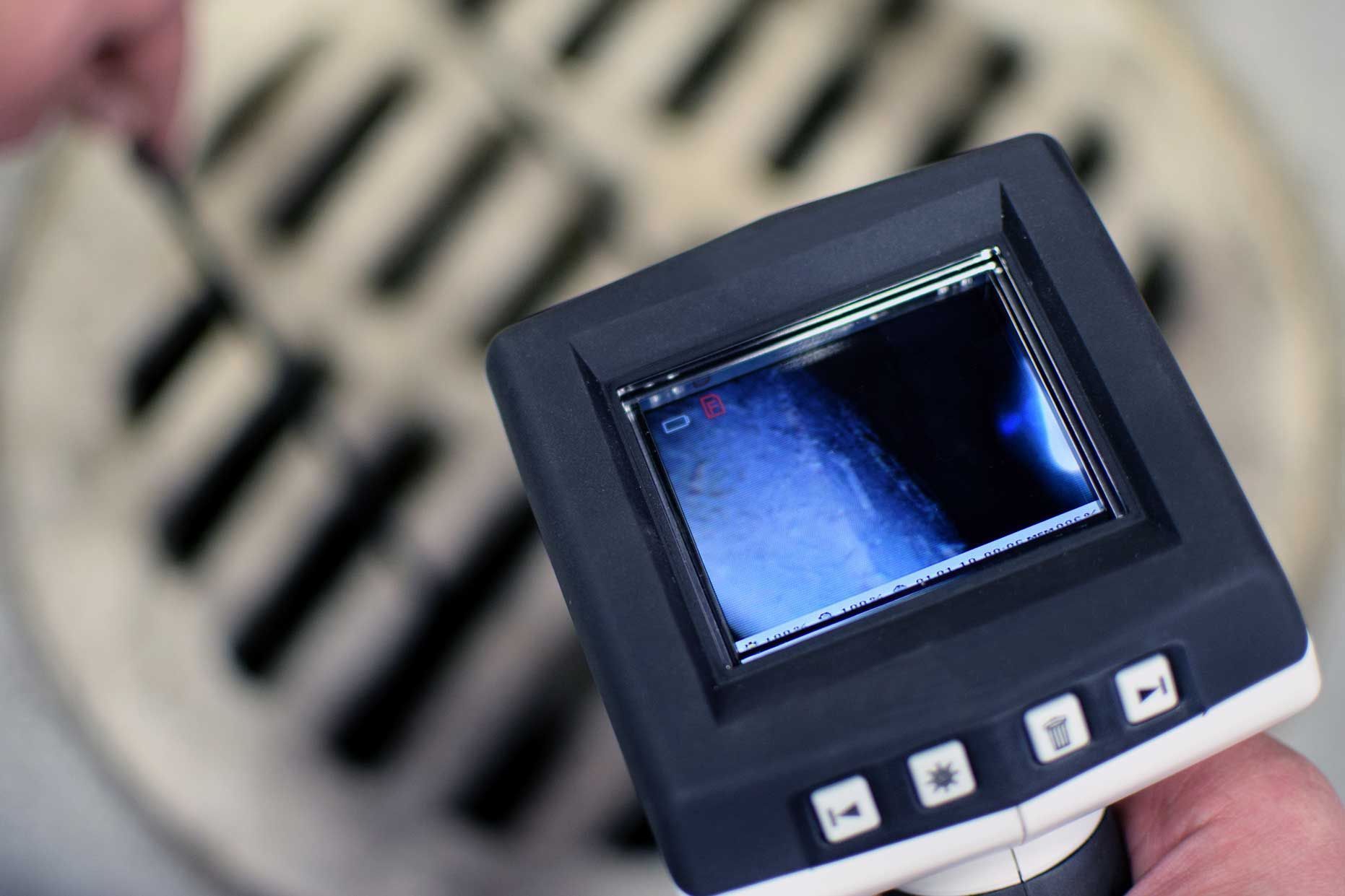 A person uses a video inspection camera over a metal grate, likely checking for blockages.
