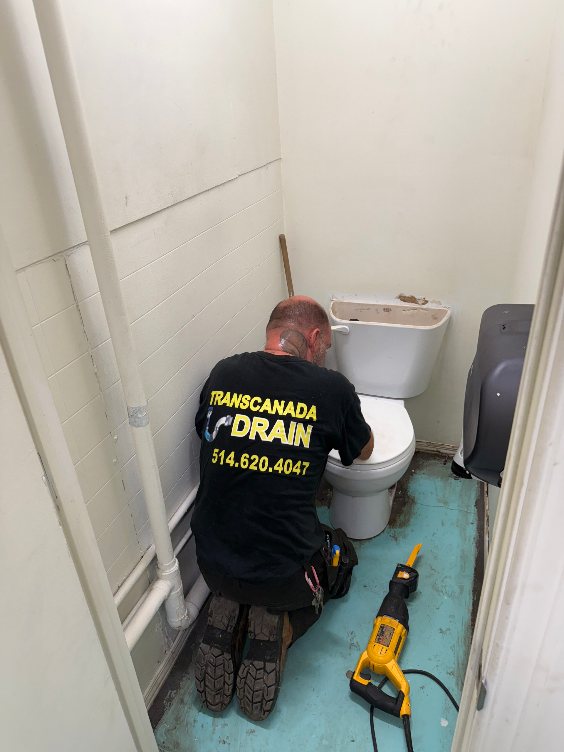 Plumber kneels by toilet, using a saw. Bathroom with green floor, white walls.