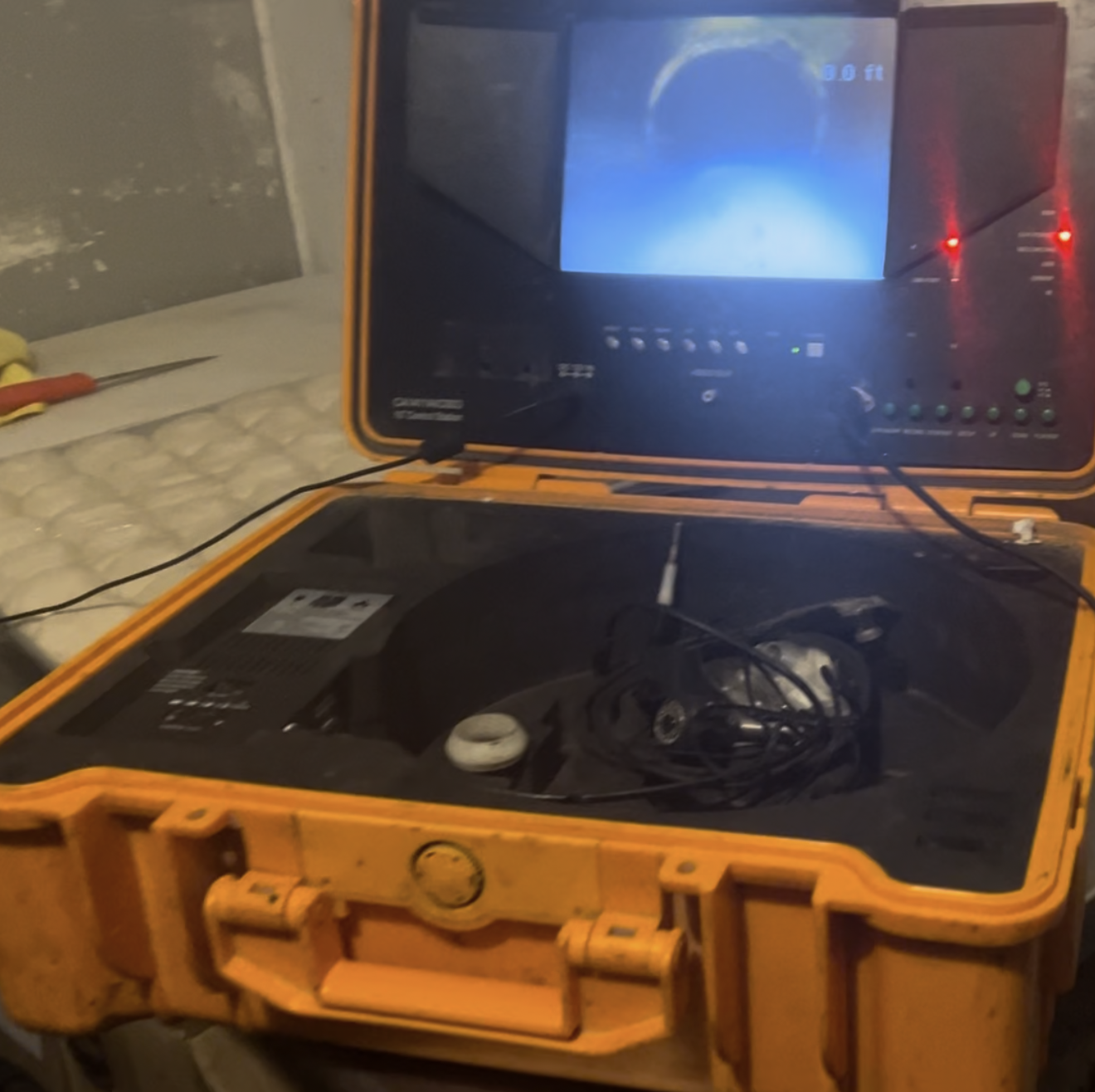 Orange video inspection camera in an open case, displaying a screen with a dark interior view.