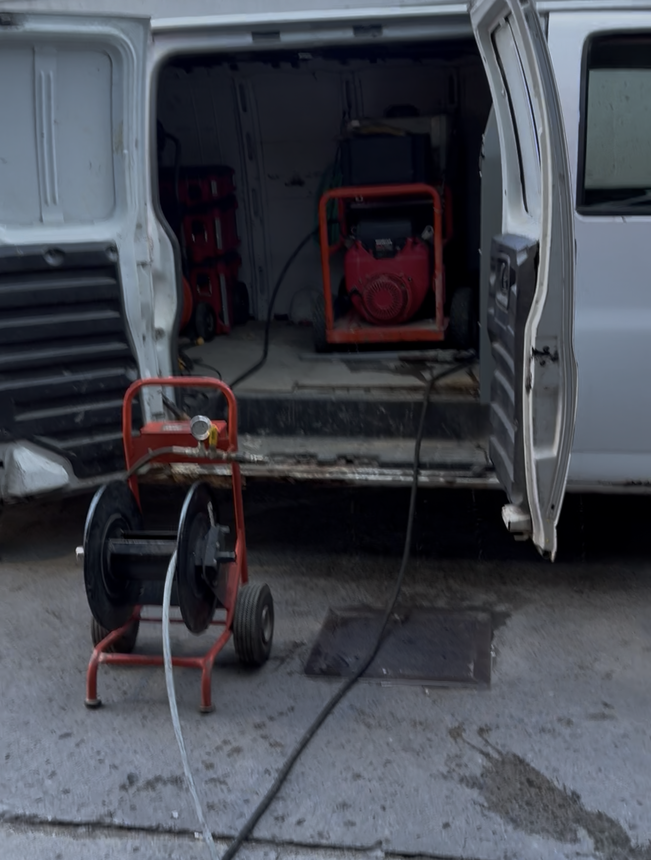 A white van with open doors. A red generator sits inside. A hose reel is outside.
