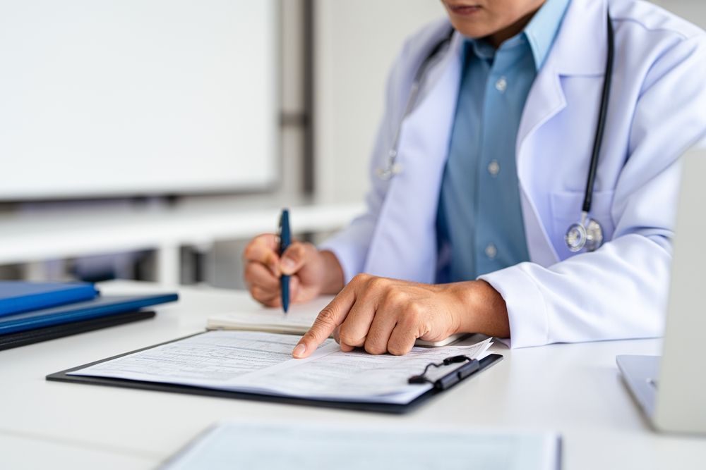 Doctor in white coat, pointing at document on clipboard, writing with pen.
