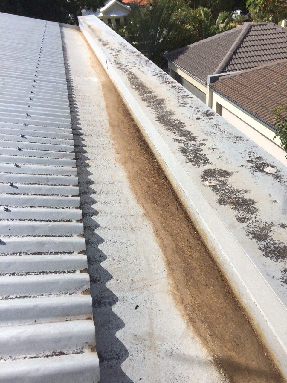 A gutter on the side of a building with a roof in the background.