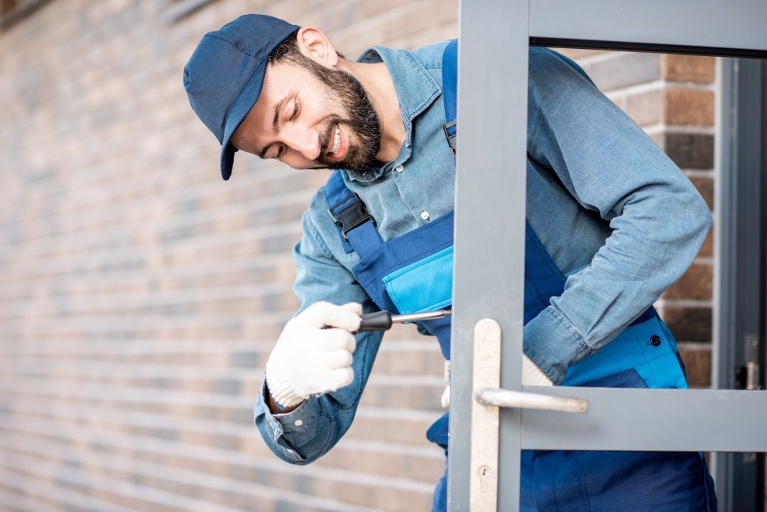 Man in blue overalls and cap fixing door lock with a screwdriver.