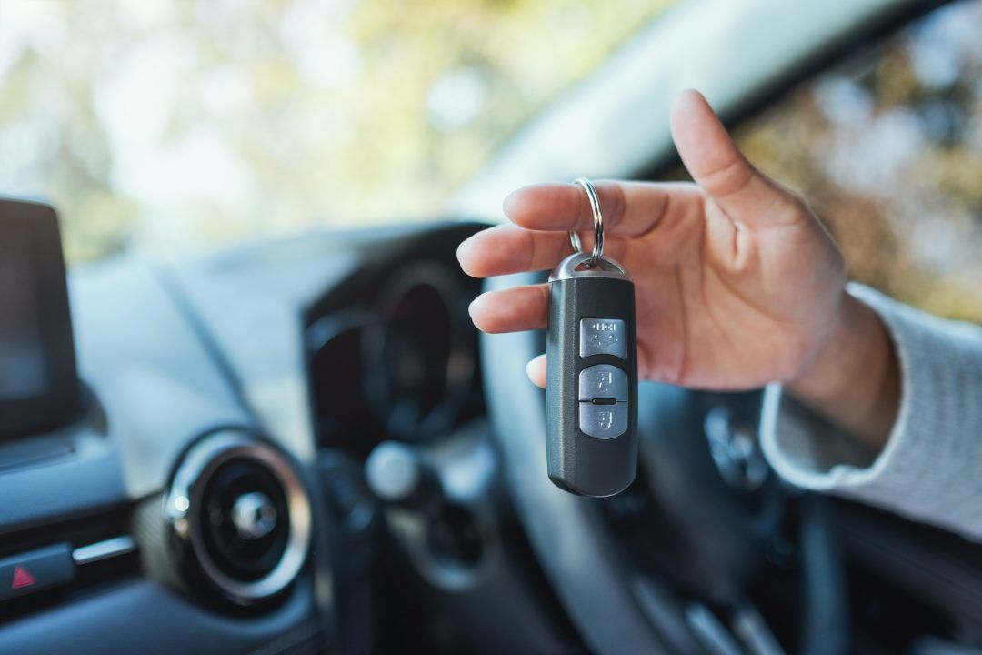 Hand holding a car key fob inside a car, ready to start the vehicle.