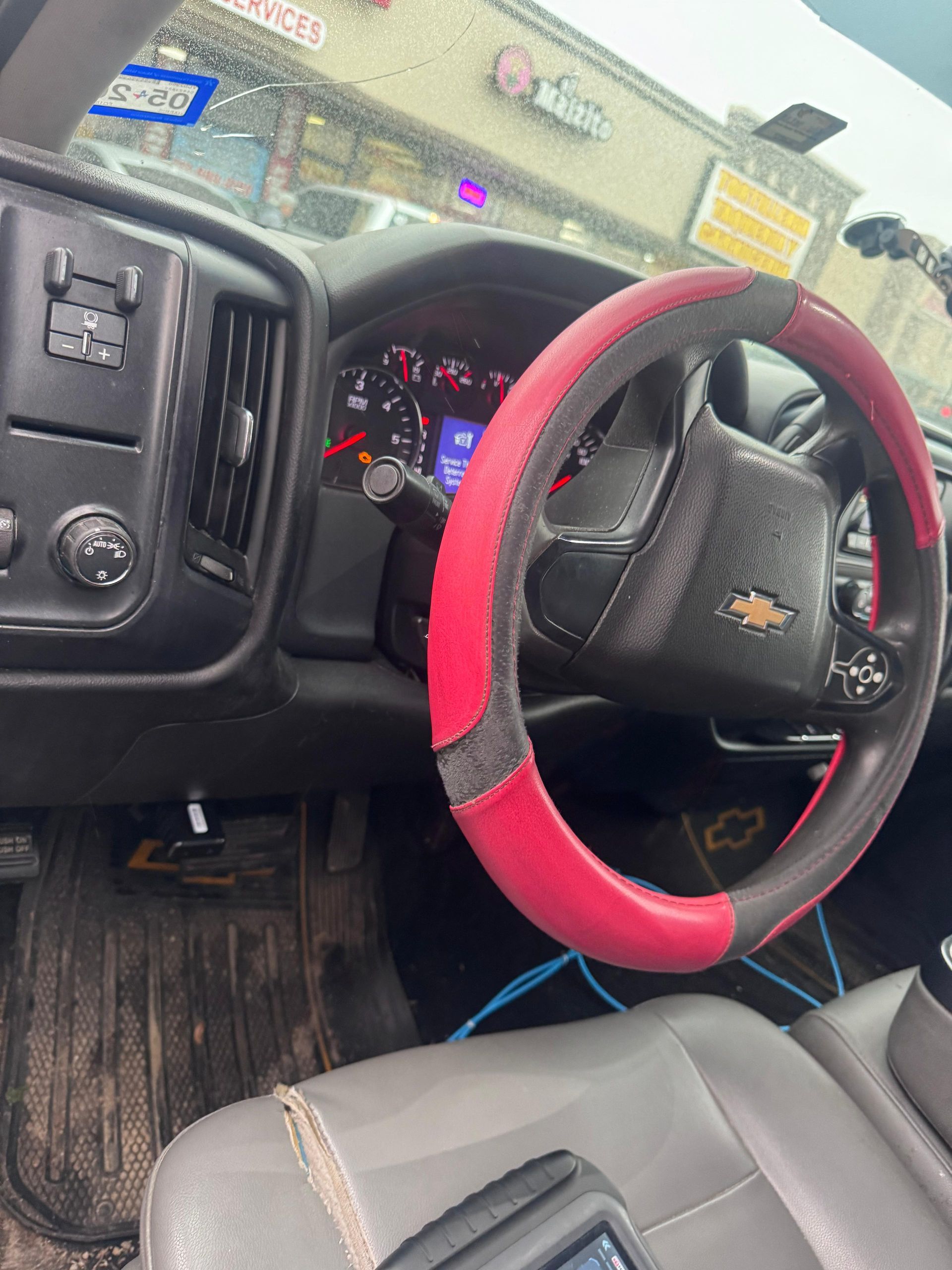 Interior of a Chevy truck. Black dashboard, red and black steering wheel cover, and gray seat.