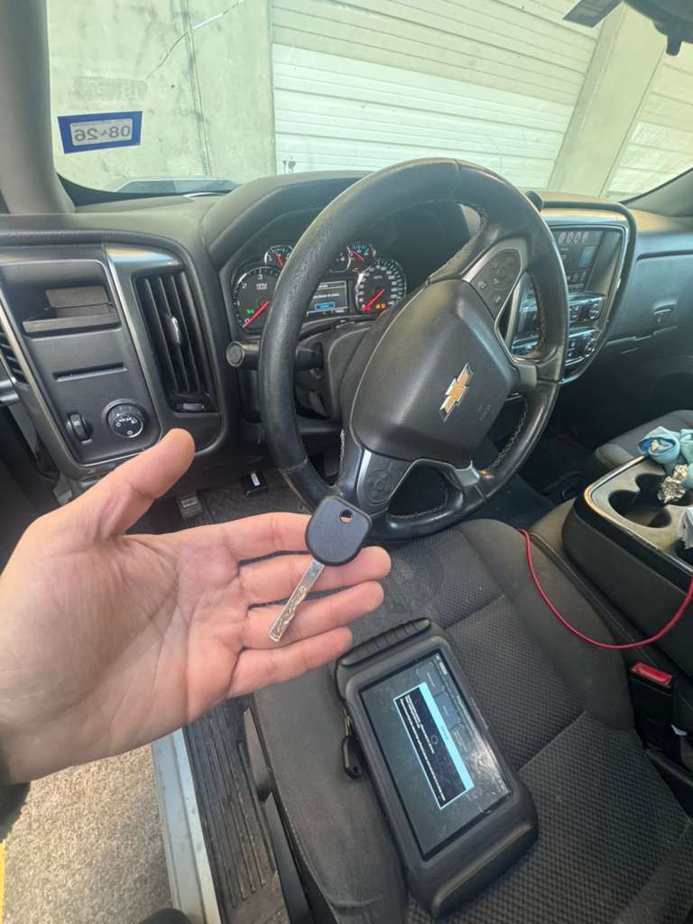 Person holding a car key and a programming device inside a Chevrolet truck.