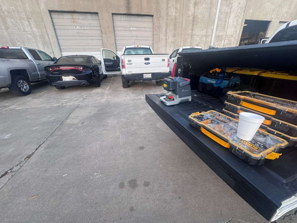 Back of a truck with tools; other vehicles in background. Gray concrete, white cup.