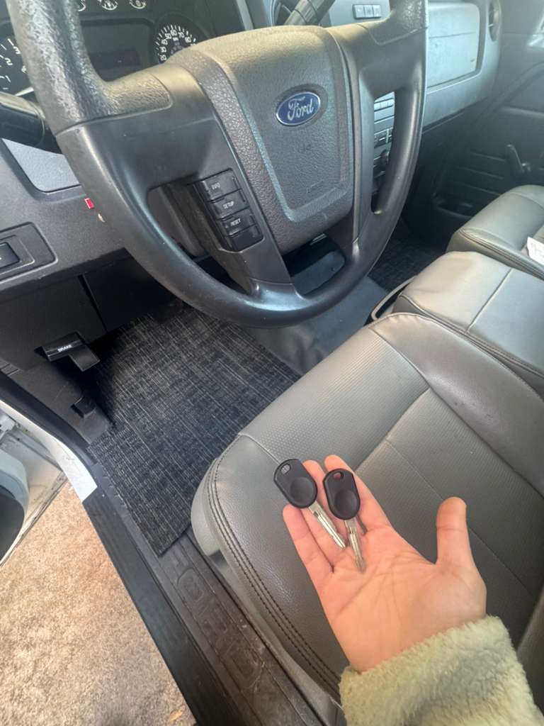 Hand holding car keys inside a vehicle's driver's seat. Steering wheel and dashboard visible.