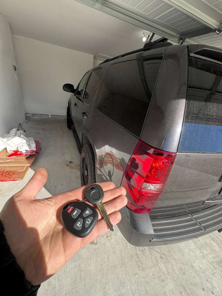 Hand holding car keys in front of a gray SUV, parked in a garage.