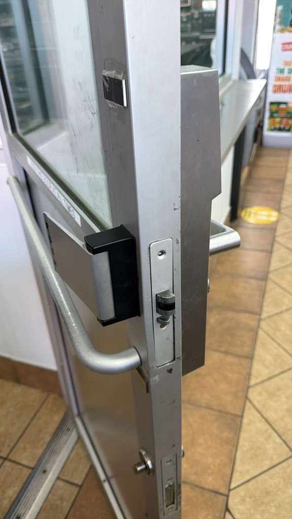 Metal door with a black handle and a locking mechanism, in a store doorway.