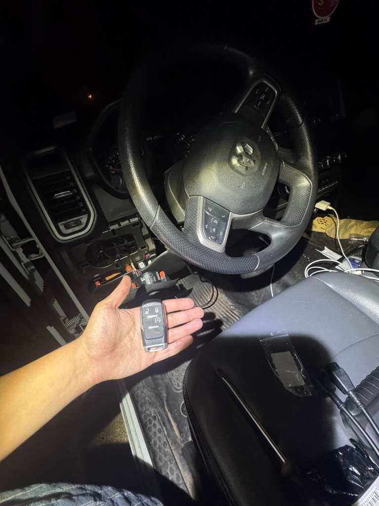 Hand holding car key inside a vehicle, steering wheel and dashboard visible.