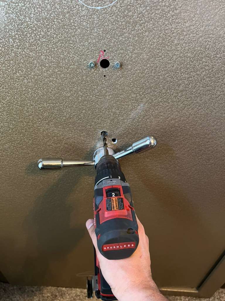 Person drilling into a safe door with a power drill.