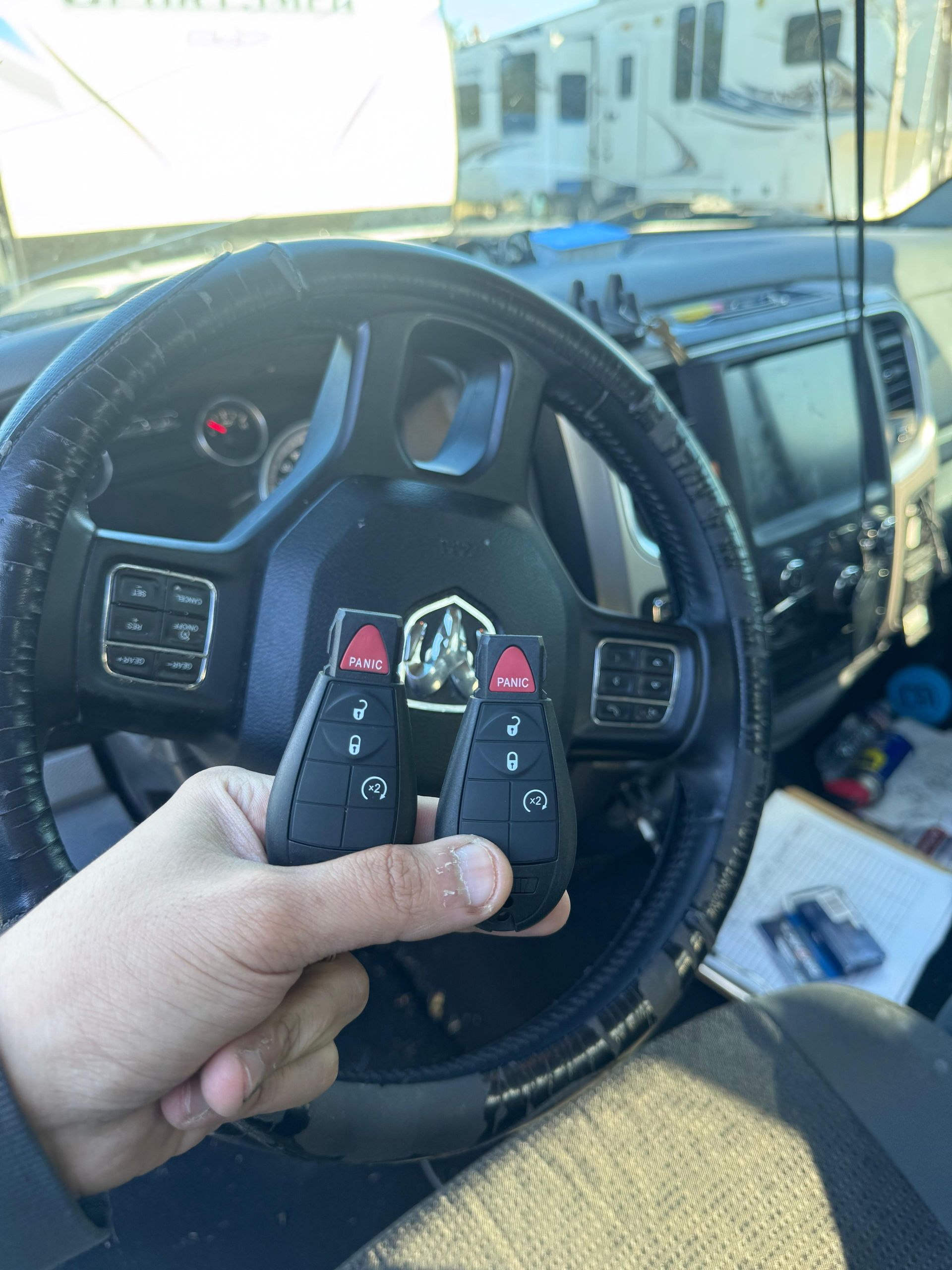 Hand holding two black car keys with red buttons, steering wheel in background.