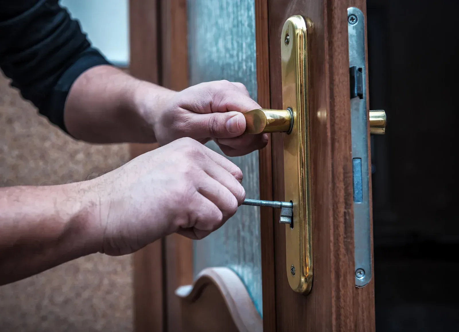Hands using a key to unlock a golden door handle on a wooden door.