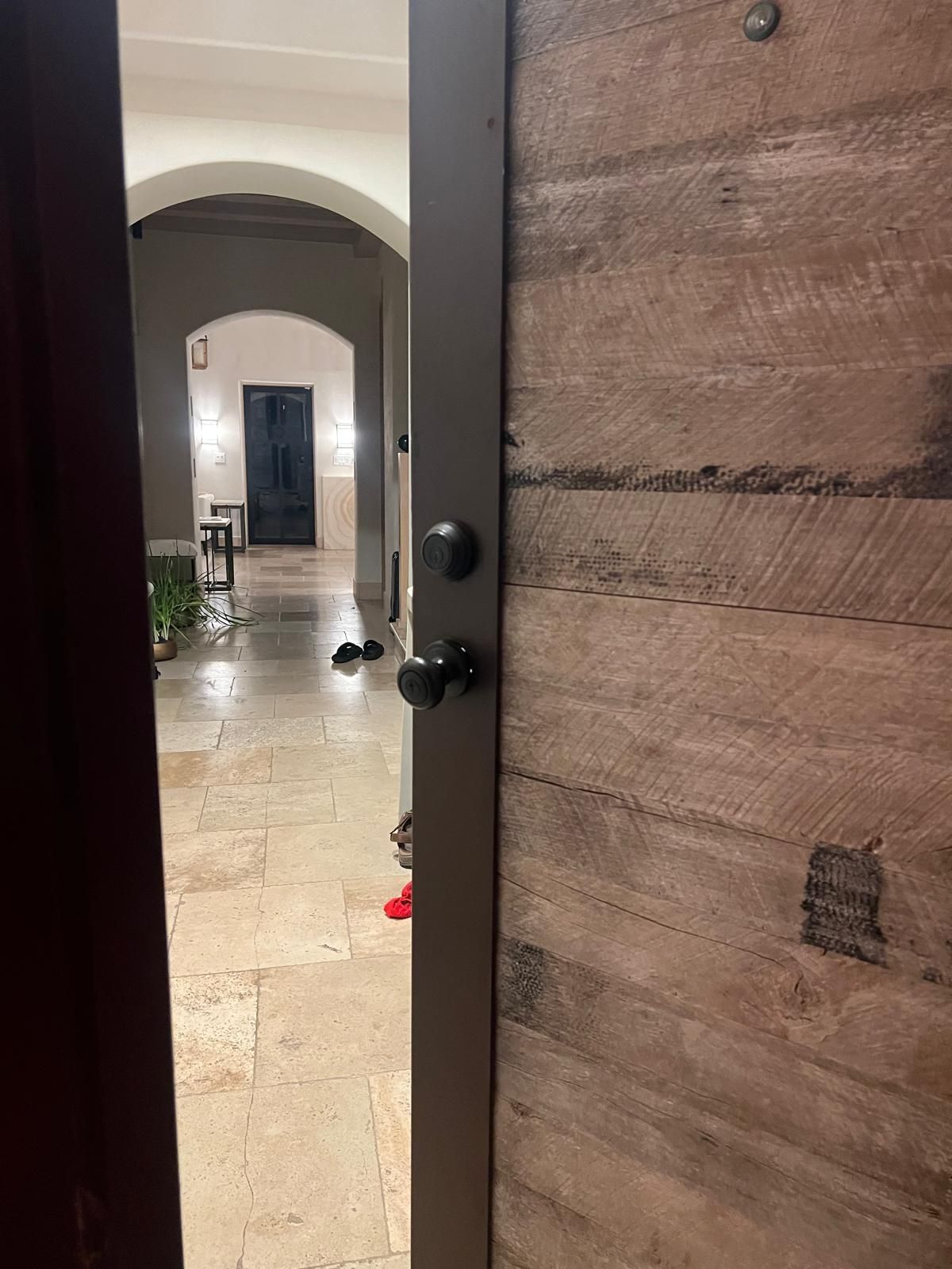 Open door revealing a hallway with arched doorway, stone floor, and dark door at the end.